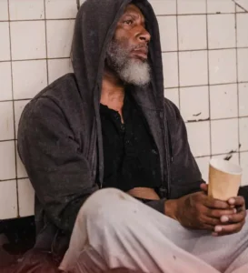 Older black man sitting agains wall with cup. Homeless