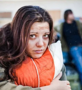 Woman holding pillow and looking at camera with very sad expression.